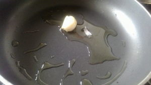 В сковороде разогреваем оливковое масло, кладем раздавленную плоской стороной ножа дольку чеснока.