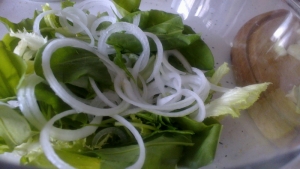 Зелень кладем в миску, добавляем авокадо и огурец, тонкими кольцами нарезаем лук. 